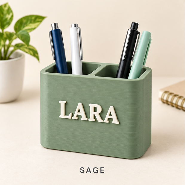 Sage green two-slot pen holder with the name LARA in raised cream letters, holding pens