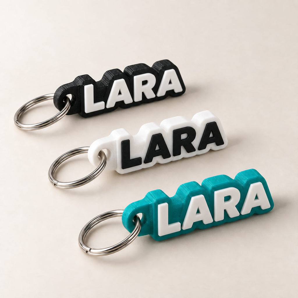 Three name keychains reading LARA in black, white and teal, with raised white letters and silver key rings
