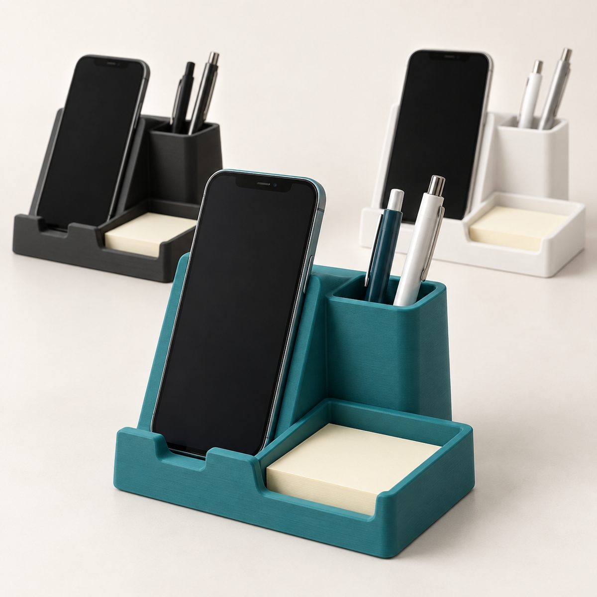 Teal phone stand holding a smartphone, with a pen cup and sticky-note tray, beside black and white versions