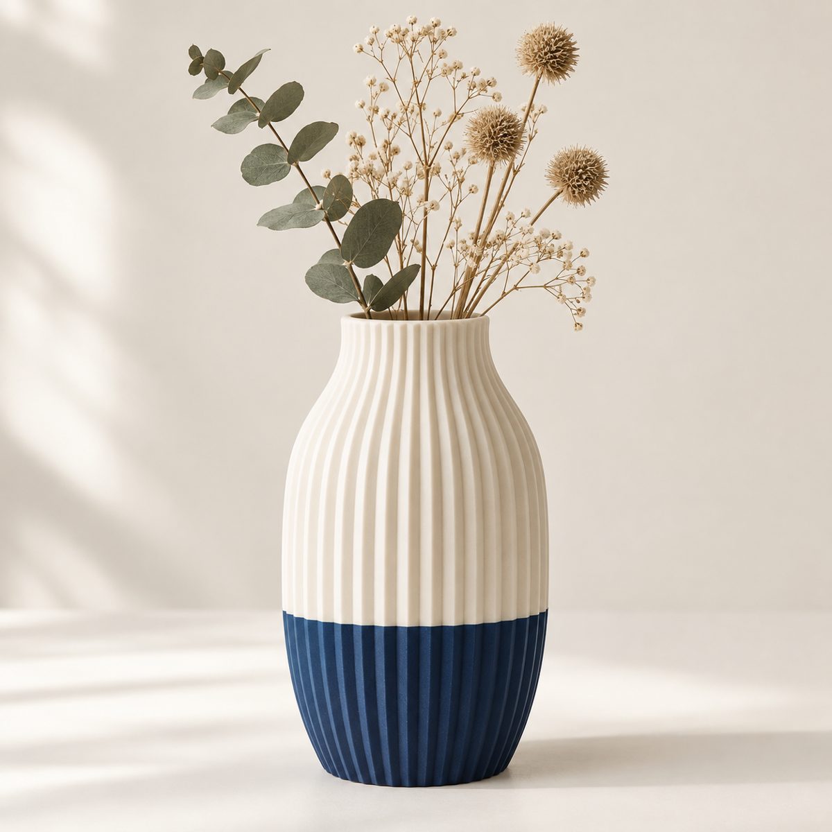 Ribbed vase, cream on top and navy at the base, holding dried flowers and eucalyptus